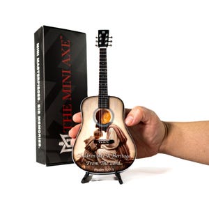 May include: Miniature acoustic guitar with a religious image on the body, displayed on a black stand. The guitar features the text "Children Are A Heritage From The Lord. Psalm 127:3". A black box with "THE MINI AXE" is in the background.