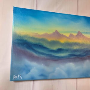Op de afbeelding: Origineel landschapsschilderij op canvas. Het kunstwerk toont een bergketen onder een lucht met een verloop van blauwe, gele en paarse tinten. De handtekening van de kunstenaar, "HAYS", is zichtbaar in de linker benedenhoek. Het schilderij roept een serene, natuurlijke sc&egrave;ne op.