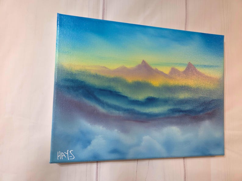Op de afbeelding: Origineel landschapsschilderij op canvas. Het kunstwerk toont een bergketen onder een lucht met een verloop van blauwe, gele en paarse tinten. De handtekening van de kunstenaar, "HAYS", is zichtbaar in de linker benedenhoek. Het schilderij roept een serene, natuurlijke sc&egrave;ne op.