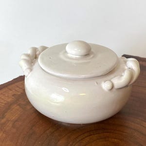 May include: A white ceramic mug with a black handle and the text "But First, Coffee" in a black, handwritten-style font. The mug is on a white surface.