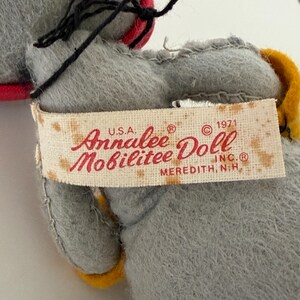 K&ouml;nnte beinhalten: Nahaufnahme einer Vintage-Annalee-Puppe. Die Puppe ist grau mit schwarzen Haaren und einem roten und gelben Akzent. Auf dem Etikett steht "Annalee Doll Mobilitee Inc. Meredith, N.H. U.S.A. &copy; 1971".