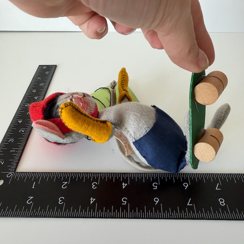 K&ouml;nnte beinhalten: Ein handgefertigtes Stofftier mit rotem Hut, gelbem Schnabel und blau-grauem K&ouml;rper. Das Spielzeug hat ein gr&uuml;nes Skateboard mit Holzr&auml;dern. Ein Lineal liegt neben dem Spielzeug und misst in Zentimetern.