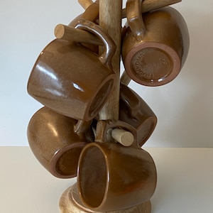 Pode incluir: Um conjunto de seis canecas de cer&acirc;mica esmaltada castanha penduradas num suporte de madeira clara em forma de &aacute;rvore. Cada caneca tem um acabamento liso e brilhante e uma pega robusta. A marca Frankoma est&aacute; estampada na base de uma caneca.