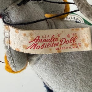 K&ouml;nnte beinhalten: Nahaufnahme eines Vintage-Annalee-Puppenetiketts. Das Etikett ist cremefarben mit den Worten "Annalee Doll Mobilitee" in roter Schrift. Das Etikett enth&auml;lt auch den Text "U.S.A. &copy; 1971 INC.&reg; MEREDITH, N.H."