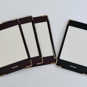 May include: Four rectangular menu covers with white inserts. Three covers are dark brown and one is black. Each cover features gold-toned metal corner protectors and the text COACH HIDE embossed in gold lettering at the bottom center of the front panel.