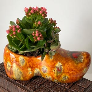 May include: A white ceramic mug with a black handle and the text "But First, Coffee" in a bold, black font. The mug is filled with a dark liquid, likely coffee, and sits on a light-colored surface.