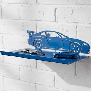 May include: A blue metal car-shaped key holder mounted on a white brick wall. The key holder has a shelf with keys and a small blue car model. The key holder is a decorative item.