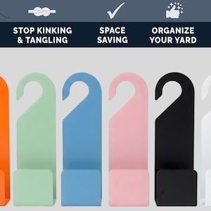 Puede incluir: Una fila de colgadores de manguera de jard&iacute;n de pl&aacute;stico de colores, en naranja, verde menta, azul claro, rosa, negro y blanco. Los colgadores tienen un gancho en la parte superior y una base rectangular. El texto en la parte superior dice "Stop Kinking & Tangling", "Space Saving" y "Organize Your Yard".
