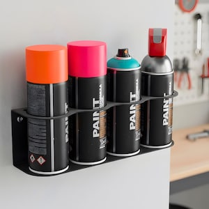 May include: A black metal spray paint can holder mounted on a white surface, holding four cans of spray paint. The cans have bright orange, pink, and teal caps. The cans are labeled "PAINT".