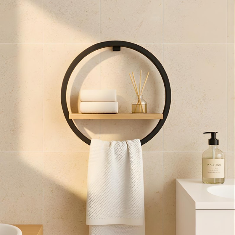 May include: A black metal circular towel rack with a wooden shelf holding two folded white towels and a glass diffuser. A white towel hangs below. A bottle of hand soap sits to the right.