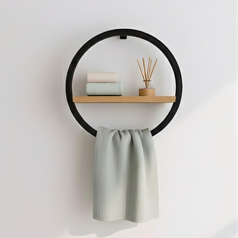 May include: A black circular wall shelf with a wooden shelf and a towel bar. The shelf holds two rolled towels, a small diffuser, and a hanging light green towel. The design is modern and minimalist.