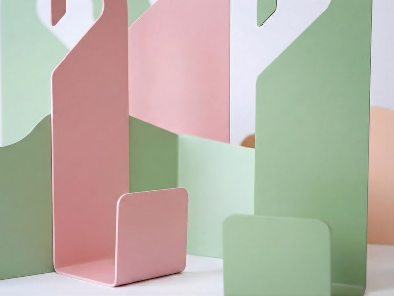 Puede incluir: Composici&oacute;n abstracta de formas met&aacute;licas en colores pastel. La imagen presenta una estructura rosa en forma de gancho y varias formas rectangulares verdes y rosas. El dise&ntilde;o es minimalista y moderno, centrado en el color y la forma.