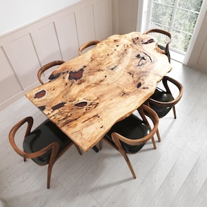 May include: A large, natural-edge wooden dining table with a light brown finish and dark red accents. Six wooden chairs with black leather seats surround the table, creating a modern dining set.