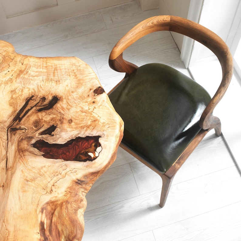 May include: A wooden chair with a dark green leather seat and a natural wood table. The table has a unique, organic shape with a reddish-brown inlay. The chair's frame is made of dark wood.
