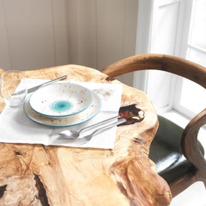 May include: A table setting featuring a white plate and bowl with a blue swirl design, a knife, fork, and spoon. The table is made of wood and has a natural, organic shape. A glass of water and a white napkin are also present.