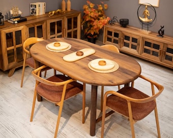 May include: A wooden oval dining table with four chairs. The table is a medium brown color and has a single central leg. The chairs have wooden frames and rust-colored upholstered seats. The table is set with placemats and small wooden bowls.