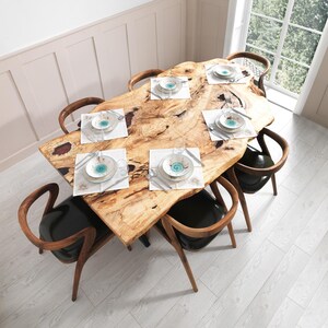 May include: A large, live-edge wooden dining table with six place settings. Each setting includes a white placemat, a patterned plate, silverware, and a glass. The table is surrounded by six wooden chairs with black leather seats.