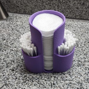 May include: A purple, three-compartment organizer for bathroom essentials. The center section holds cotton pads, while the side compartments contain cotton swabs. The organizer sits on a speckled countertop, providing a neat storage solution.