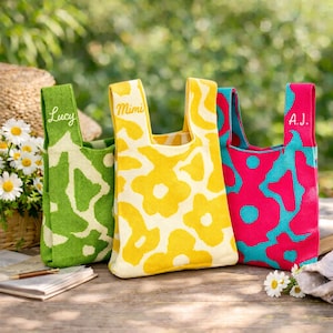 May include: Three knit tote bags with floral patterns. The green bag features the name Lucy, the yellow bag features the name Mimi, and the pink and blue bag features the name A.J. Each bag has two integrated handles and a soft, textured knit fabric.