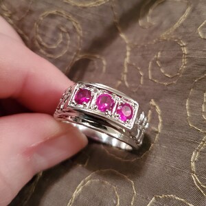 May include: A silver band ring with three pink gemstones set in a row.