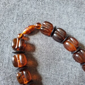 May include: A close-up of a bracelet featuring amber-colored, square beads with rounded edges. The beads are separated by small, black, circular spacers. The bracelet has a warm, earthy tone, with the beads appearing translucent.