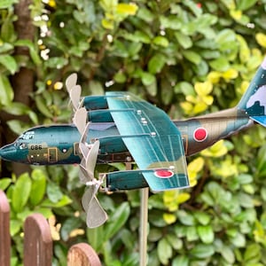 Può includere: Un modello dettagliato di aereo con un design mimetico verde e verde acqua. Il modello presenta quattro eliche, un emblema a cerchio rosso e il numero "086" sul lato. Le ali e la coda hanno un motivo mimetico. Il modello è esposto all'aperto.