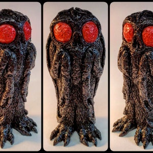 May include: A black, textured figurine with large, red eyes. The figure has a detailed, rough surface and clawed feet. The design is reminiscent of a mythical creature or monster, with a unique and imposing presence.