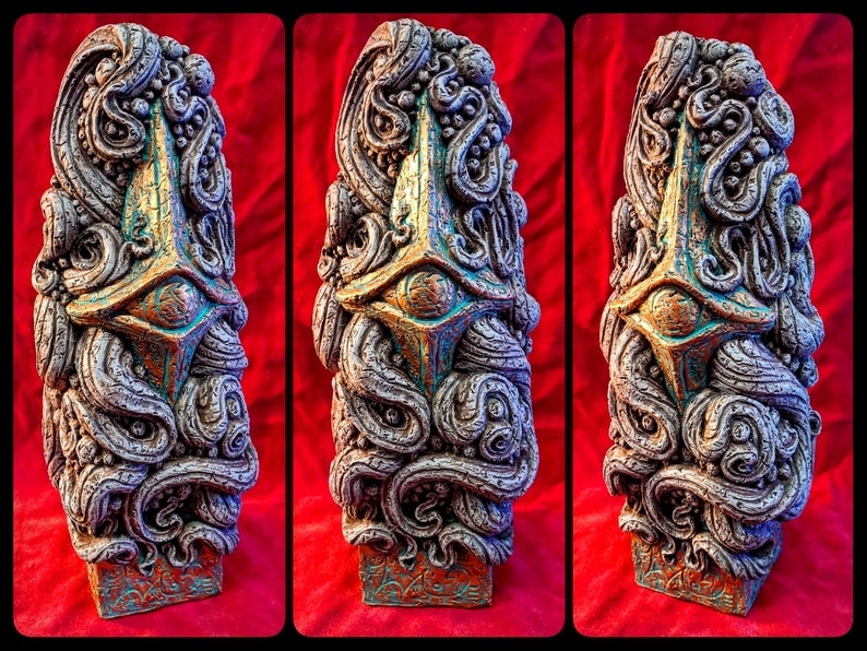 May include: A decorative, hand-painted, ceramic sculpture with a gold and teal color scheme. The sculpture features a stylized eye and intricate, swirling patterns.