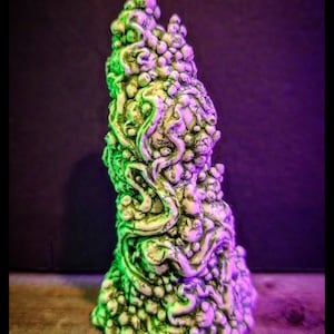 Könnte beinhalten: Eine einzigartige, abstrakte Skulptur mit strukturierter Oberfläche. Das Stück ist überwiegend cremeweiß mit grünen und violetten Akzenten und weist knollenförmige Formen und wirbelnde, organische Formen auf. Die Skulptur steht vor einem dunklen Hintergrund.