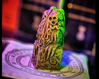 May include: A detailed, textured, green and brown resin sculpture of a Cthulhu-like creature. The sculpture is a small, tabletop piece.