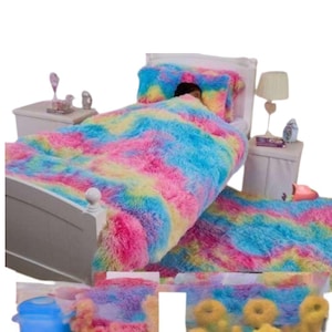 May include: A bed with a fluffy, colourful comforter and pillow set. The bedding features a vibrant mix of pink, blue, yellow, and white, creating a rainbow effect. The bed is white, and a person is under the covers.