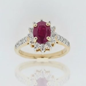 May include: A gold ring with an oval ruby centre stone, encircled by a halo of small diamonds. The band is also set with diamonds, creating a sparkling effect. The ring is set against a white background.