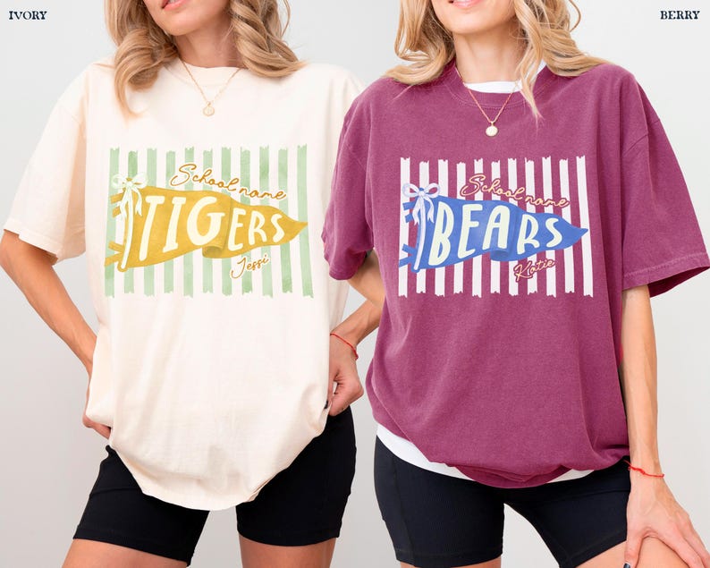 May include: Two short-sleeve crewneck t-shirts, one ivory and one berry, each featuring a central graphic of a vertical striped background with a pennant banner. The ivory shirt displays the text TIGERS, and the berry shirt displays the text BEARS.