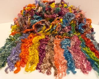 May include: A collection of multi-colored, curly, long-staple fiber locks. The fibers feature a vibrant spectrum of hues including bright yellow, orange, pink, purple, blue, and green, arranged in a dense, textured pile with loose, cascading curls.