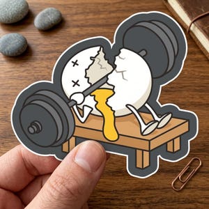 May include: A sticker featuring a cartoon egg lifting weights on a bench. The egg is cracked open, with yolk dripping out. The barbell is black, and the bench is brown. The sticker has a black border.