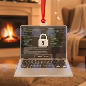 May include: Laptop-shaped ornament with a red ribbon for hanging. The screen displays a padlock icon and lines of code. The text "Your Name" is below the screen. The keyboard is visible at the bottom of the ornament.