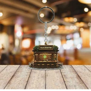 May include: A keychain featuring a miniature replica of "Ivan's Irish Pub." The pub model is detailed with a bar, stools, and shelves of bottles. The keychain has a silver ring and chain, and the pub sign is visible.