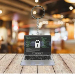 May include: A silver laptop keychain with a screen displaying a white padlock icon and lines of code. The screen also has the text "Your Name". The keychain hangs from a silver ring and chain.