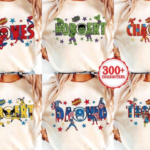 May include: Cream-colored t-shirts with personalized names in a Marvel comic book style. Each shirt features a different name, such as "James", "Robert", and "Charles", with corresponding superhero graphics and star accents.