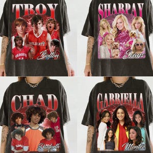 May include: Four dark gray t-shirts featuring High School Musical characters. Each shirt has a different character's name in a red and white font, along with images of the actors. The names are Troy, Sharpay, Chad, and Gabriella.
