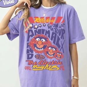 Peut inclure: T-shirt violet Comfort Colors avec un graphisme d'Animal des Muppets et le texte "Killer Coaster On Tour Animalx" et "The Electric Mayhem ORL FL". Le t-shirt a un aspect vintage et vieilli.