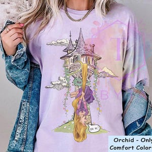May include: Orchid-colored Comfort Color shirt featuring a cartoon illustration of a tower with a long-haired character hanging upside down. The character is wearing a purple dress and has long blonde hair. The shirt has the text "Oh Hi!" in a speech bubble.