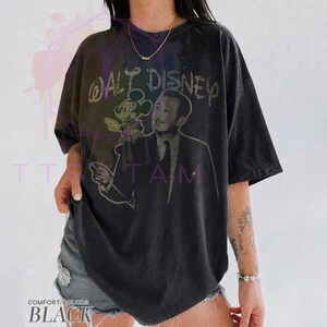 Może przedstawiać: Czarny t-shirt z kr&oacute;tkim rękawem z grafiką przedstawiającą Walta Disneya i Myszkę Miki. Napis "WALT DISNEY" jest nadrukowany postarzaną czcionką nad postaciami. Koszulka ma okrągły dekolt i luźny, swobodny kr&oacute;j.
