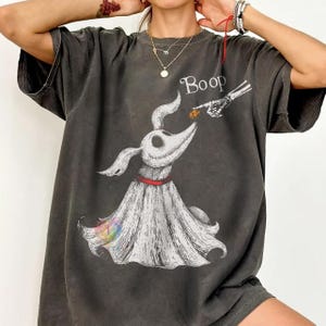 Könnte beinhalten: Ein anthrazitfarbenes Kurzarm-T-Shirt mit einer Grafik eines weißen Geisterhundes mit rotem Halsband. Eine skelettierte Hand reicht herab, um die Nase des Hundes zu berühren, darüber steht der Text Boop. Das Design wirkt wie eine Skizze.