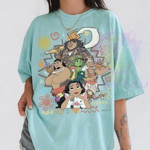 May include: A light blue t-shirt featuring a colorful graphic of characters from a popular animated movie. The design includes a variety of characters, a large hook, and decorative tribal patterns. The shirt is a comfortable, casual style.