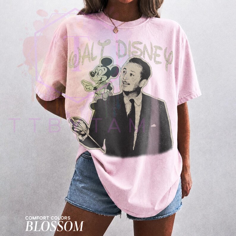 Może przedstawiać: Jasnor&oacute;żowy t-shirt z kr&oacute;tkim rękawem z nadrukiem graficznym przedstawiającym Walta Disneya i Myszkę Miki. Napis WALT DISNEY znajduje się nad postaciami w wyblakłym stylu. Koszulka ma okrągły dekolt i luźny kr&oacute;j, zestawiona z niebieskimi szortami.