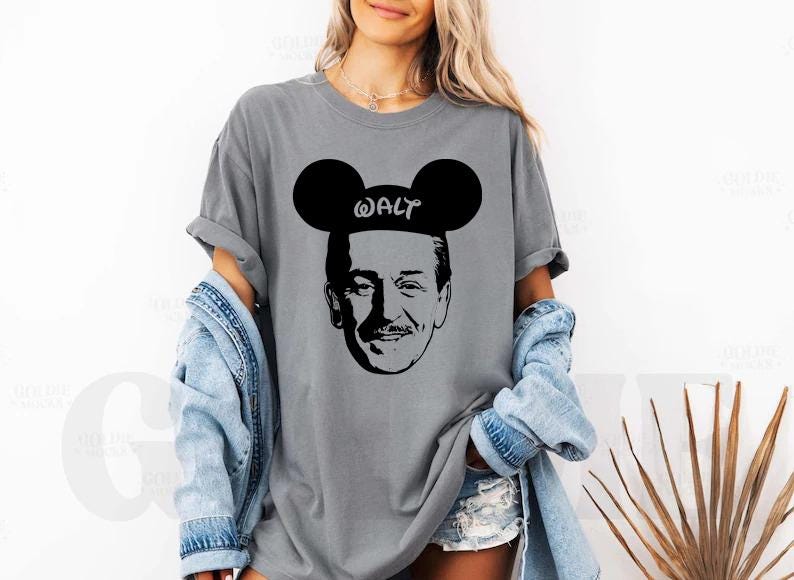 Puede incluir: Camiseta gris con un gr&aacute;fico negro de Walt Disney con orejas de Mickey Mouse y la palabra "WALT". La camiseta tiene un corte holgado y se combina con una chaqueta vaquera y pantalones cortos.
