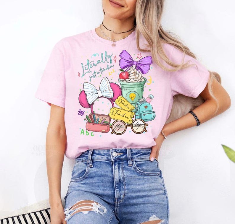 May include: Pink t-shirt with a colorful graphic design featuring a Minnie Mouse-inspired bow, a coffee cup with whipped cream, a backpack, and the text "Literally just a teacher". The design includes pencils, glasses, and apple.