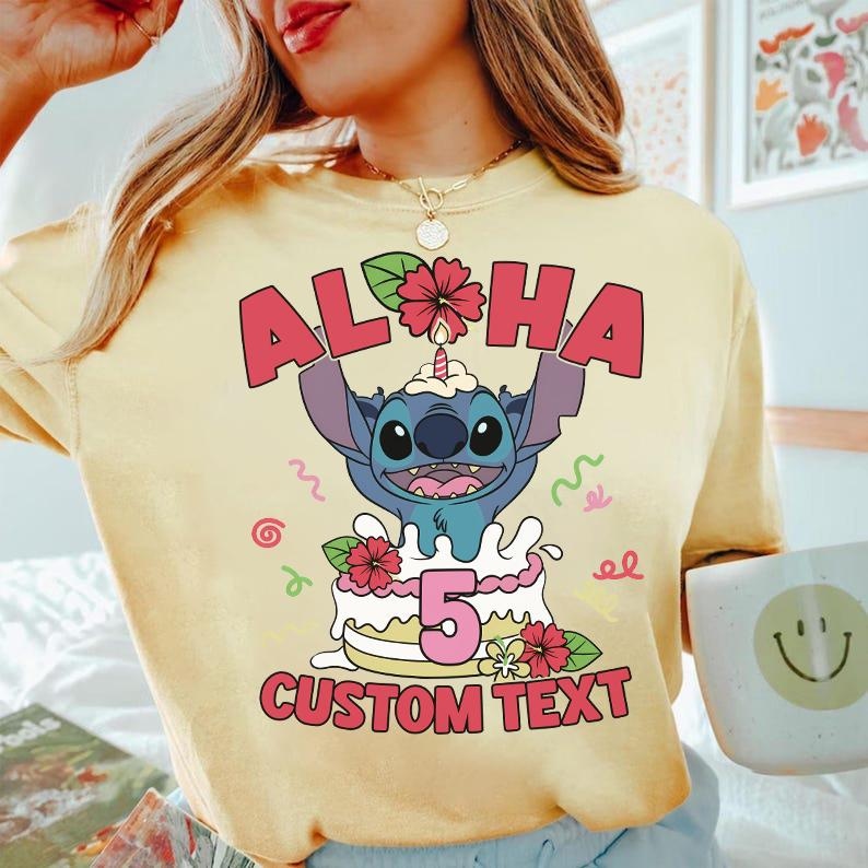 May include: Yellow t-shirt featuring a cartoon character with the text "ALOHA" above a birthday cake with the number "5" and the words "CUSTOM TEXT". The design includes flowers and colorful swirls.
