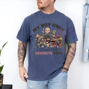 K&ouml;nnte beinhalten: Ein blaues kurz&auml;rmeliges T-Shirt mit einem Grafikdruck verschiedener Spielzeugfiguren und dem Text "MY BOY ONLY" oben sowie "Break His FAVORITE TOYS" unten in brauner und orangefarbener Schrift, mit Rundhalsausschnitt und lockerer Passform.